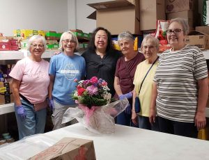 a group of volunteers from Millers Grant pose with a site coordinator from CCC. A bouquet of flowers sits on a table in front of them.